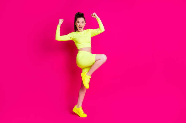 Full size profile photo of astonished sexy young lady stand fists leg up yell dress sport suit footwear isolated on vibrant pink color background - Photo, image