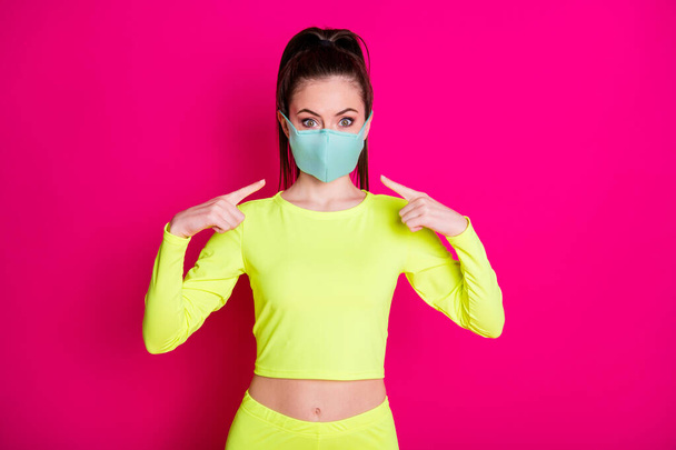 Portrait photo of girl pointing at medical protective mask wearing sportswear ponytail isolated on vibrant fuchsia color background - Foto, Imagen