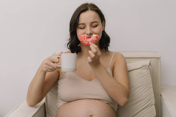 Pregnancy and nutrition. Pregnant woman enjoying donuts and tea. - Photo, image
