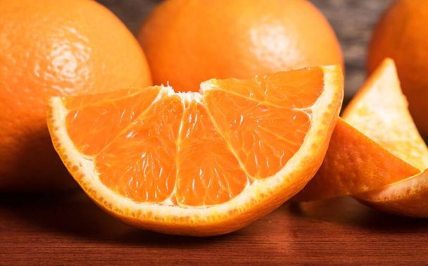 Frische Orangenscheibe und ganze Orange auf Holztisch. Orangen sind eine hervorragende Quelle für Ballaststoffe und Vitamin C. Antioxidantien in Orangen schützen die Haut vor Schäden durch freie Radikale und stoppen vorzeitige Alterung.. - Foto, Bild