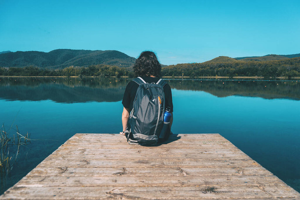 女の子は晴れた日にバニョレス湖の端に座って水に反映された風景で - 写真・画像