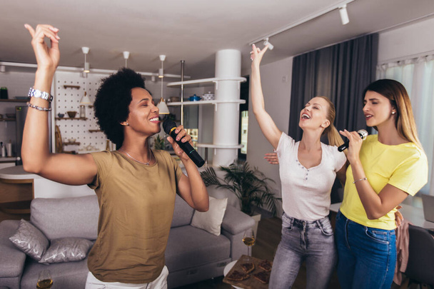 Fiatal nők csoportja szabadidőt tölt karaoke-ban, énekel és szórakozik együtt, barátokkal, otthon. - Fotó, kép