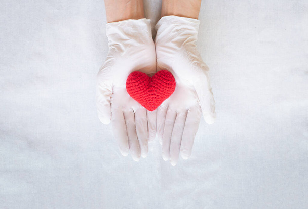 Ruce s rukavicí drží červené srdce na bílém pozadí, kopírovat prostor. Koncepce zdravotní péče, zdraví srdce, kardiologie, plán pojištění, dárcovství orgánů, den lékaře, světový den srdce. hypertenzní onemocnění. - Fotografie, Obrázek