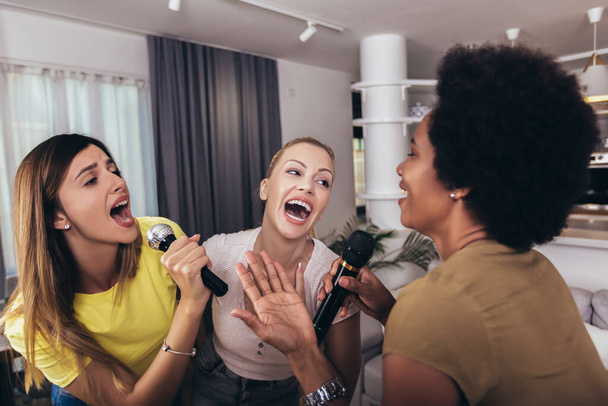Groep jonge vrouwen brengen vrije tijd door in karaoke, zingen en plezier hebben samen, met vrienden, thuis. - Foto, afbeelding