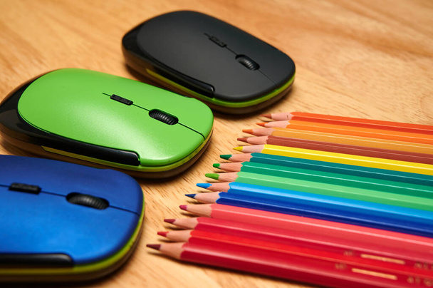 A closeup shot of multi-colored pencils and computer mouses on a wooden table - Fotoğraf, Görsel