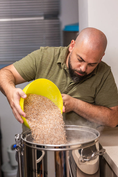 hombre vierte cebada y malta de trigo en la tetera para hacer cerveza - Foto, imagen