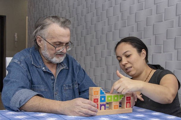 Een oudere gepensioneerde man en een vrouw van middelbare leeftijd spelen een bordspel aan een tafel. Mensen ontwikkelen logisch denken, vrije tijd voor gepensioneerden, home entertainment tijdens de quarantaineperiode. - Foto, afbeelding