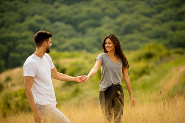 Happy young couple in love walking through grass field on a summer day - Foto, Imagen