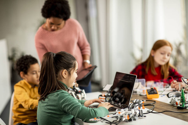 Ryhmä onnellisia lapsia afroamerikkalaisen naisopettajansa kanssa, jolla on kannettavan tietokoneen ohjelmointi sähköisiä leluja ja robotteja robotiikan luokkahuoneessa - Valokuva, kuva