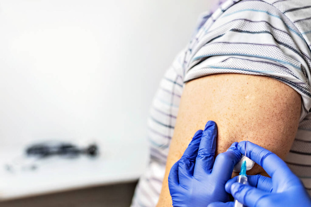 Ένας γιατρός εμβολιάζει έναν άνθρωπο κατά του ιού της στέψης σε μια κλινική. Κοντινό πλάνο. Η έννοια του εµβολιασµού, της ανοσοποίησης, της πρόληψης έναντι του Covid-19 - Φωτογραφία, εικόνα