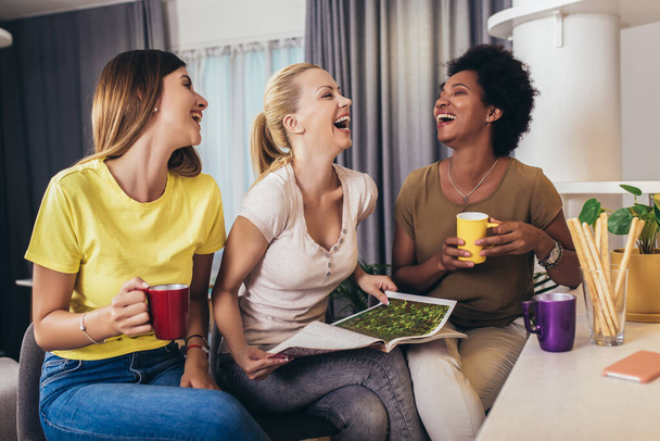Три молодих красивих усміхнених жінок читають журнал вдома
. - Фото, зображення