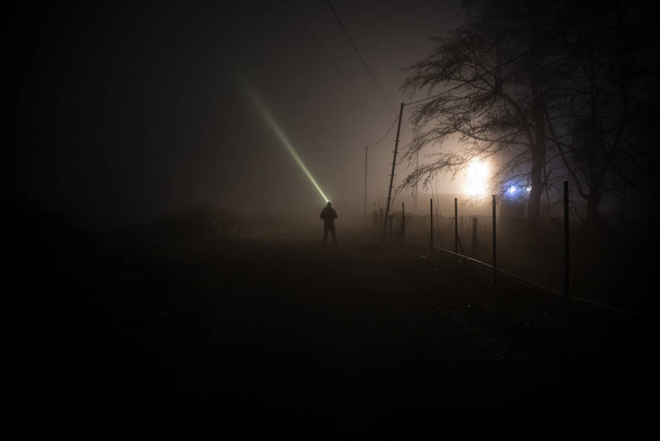 Silhouet van een persoon die met licht in het donkere bos staat. Horror Halloween concept. vreemd silhouet in een donker spookachtig dorp - Foto, afbeelding