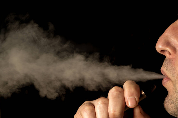 Κοντινό πλάνο σε έναν άνθρωπο που εκπνέει ατμό από ένα ηλεκτρονικό τσιγάρο - Φωτογραφία, εικόνα