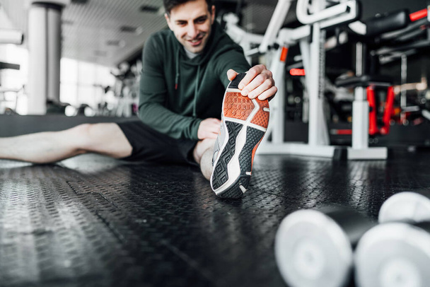 Close up focus of male athlete on the floor reaching for the tip of his leg, stretching before training. Sports lifestyle. - Фото, изображение