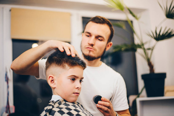 Cabeleireiro barbearia e pequeno menino sentado em uma cadeira - Foto, Imagem