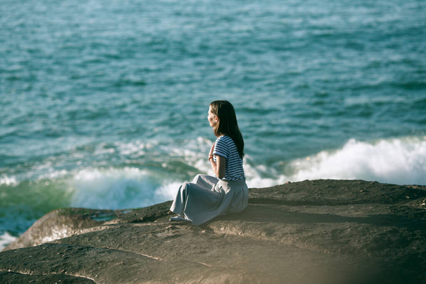 Dziewczyna medytująca na skałach na plaży morskiej. Joga i sprawność. - Zdjęcie, obraz
