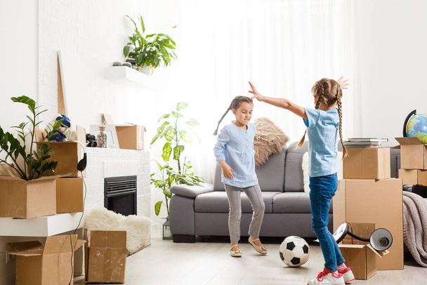 dvě malé dcery oslavující stěhování, nadšené stěhováním do nového domu, smějící se obývací pokoj s lepenkovými krabicemi - Fotografie, Obrázek