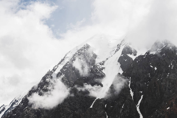Paisagem alpina minimalista atmosférica com glaciar pendurado no pico da montanha rochosa nevada. Nuvens baixas entre montanhas cobertas de neve. Serac na borda glaciar. Majestoso nevoeiro nebuloso cenário em alta altitude. - Foto, Imagem