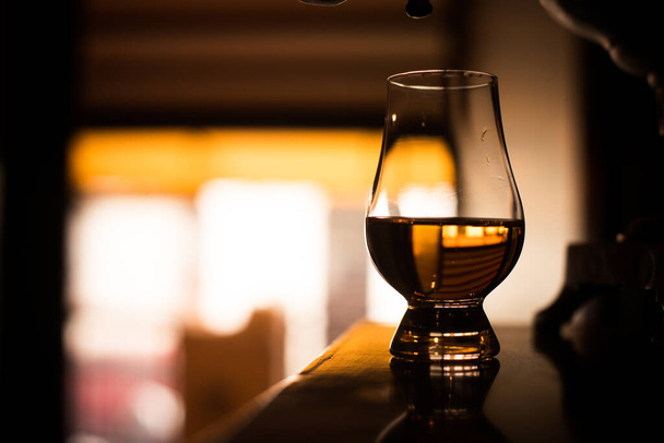 Color plano de un vaso de whisky Glencairn sobre una mesa de madera, con poca profundidad de campo. - Foto, imagen