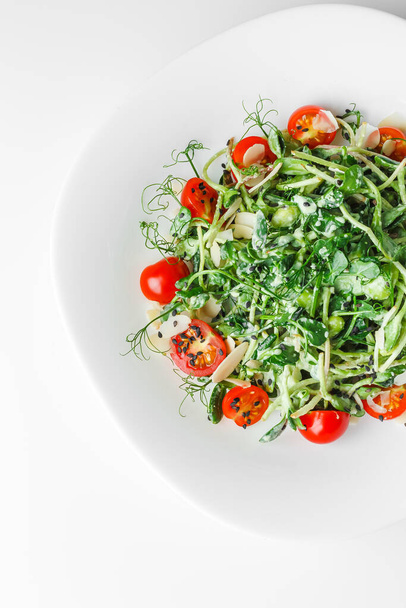 Lichte verse salade met microgroene radijs spruitjes, kerstomaten, zwarte sesam op witte plaat, witte achtergrond. Concept veganistisch en gezond eten. - Foto, afbeelding