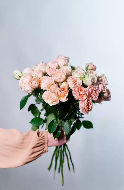 灰色の背景に孤立したバラの花の美しい花束を保持する女性の手。お祝いの花の花束 - 写真・画像