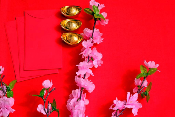 中国の旧正月春祭りは、梅の花と赤の背景に赤いパケットと金のインゴットを飾る。中国語翻訳:幸運、幸運、富、お金の流れ.  - 写真・画像