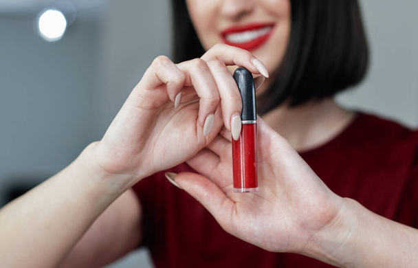 Closeup candid portrait of cheerful young woman with red lips smiling broadly showing her favorite lipstick. Brunette female with red lips making an online tutorial with beauty product. - Foto, immagini