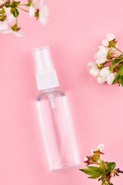 Flasche mit transparenter Flüssigkeit. Alkohol Händedesinfektionsmittel über rosa Hintergrund mit Blumendekoration - Foto, Bild