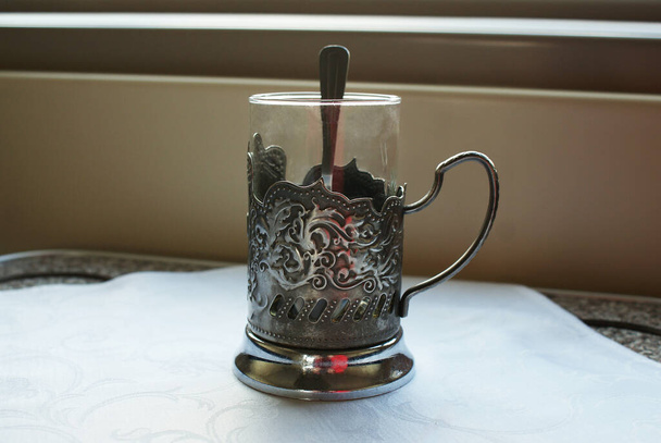 Стакан с чайной ложкой в держателе для чашки на столе в поезде. - Фото, изображение