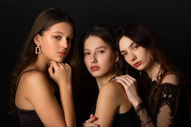  three beautiful young women with makeup and hairstyle on a black background - Фото, изображение