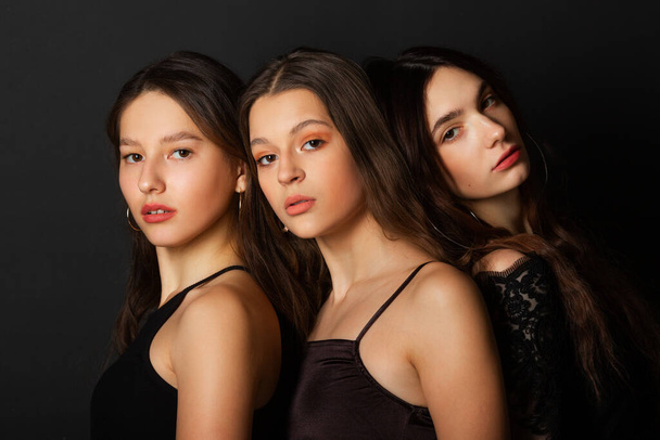  three beautiful young women with makeup and hairstyle on a black background - Foto, afbeelding