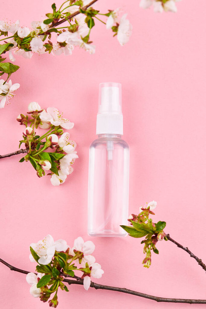 bouteille avec liquide transparent. désinfectant pour les mains en alcool sur fond rose avec décoration florale - Photo, image