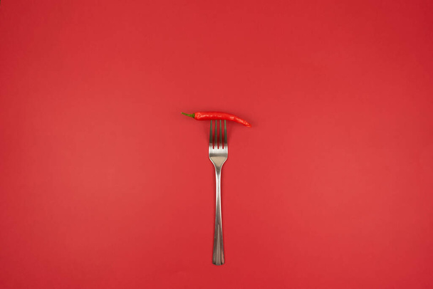 A red hot chili pepper on a fork on a red background - Фото, зображення