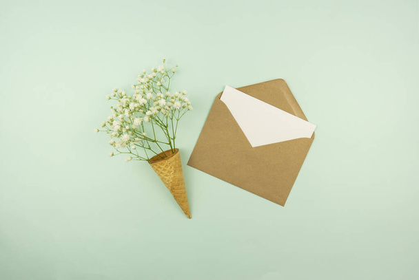 Spring is coming concept. A blank in a brown envelope with fresh flowers in a waffle cone. Mock up - Fotó, kép