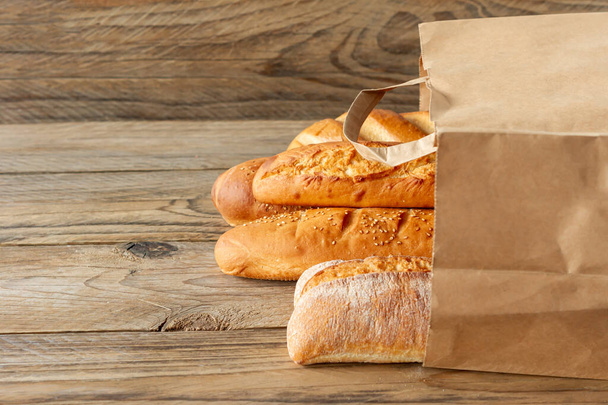 arranged french baguettes in paper bag and wheat on rustic wooden tabletop. - Fotoğraf, Görsel