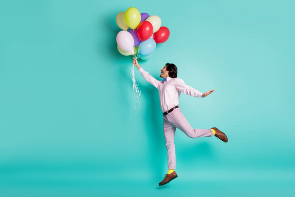Portrait of jumping young man hold colorful helium balloons wear formal outfit yellow socks isolated on turquoise background - Valokuva, kuva