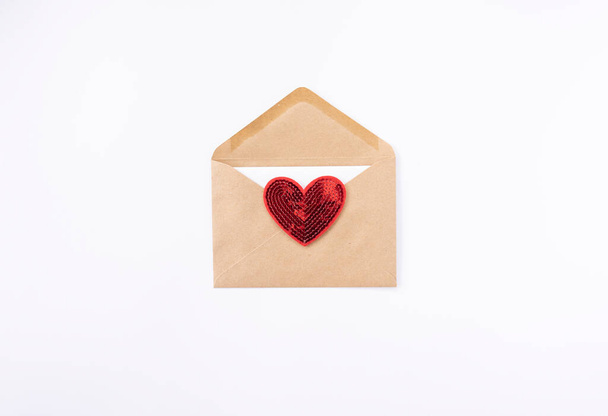 Un corazón rojo yace en un sobre marrón para el Día de San Valentín - Foto, Imagen