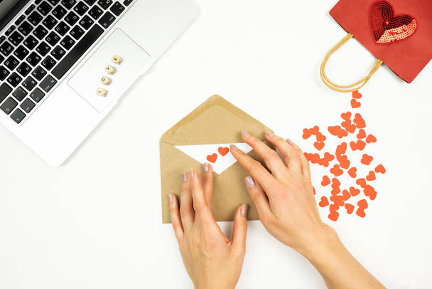Sevgililer Günü için kahverengi bir zarfı kırmızı kalplerle süsleyen bir kadın. - Fotoğraf, Görsel