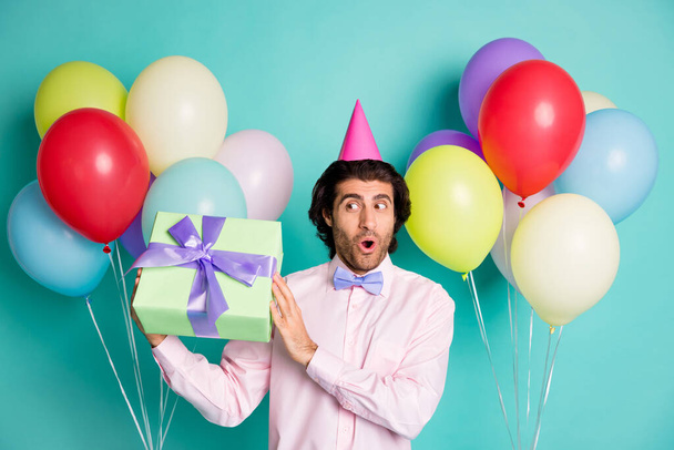 Photo of curious gentleman hold giftbox colorful helium balloons wear cone cap isolated on turquoise color background - Fotó, kép