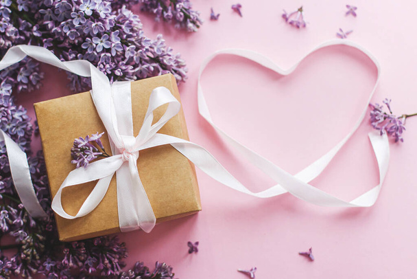 Happy valentines day and mothers day flat lay. Lilac flowers, gift box and heart ribbon on pink paper. Purple lilac bouquet and craft present - Фото, зображення