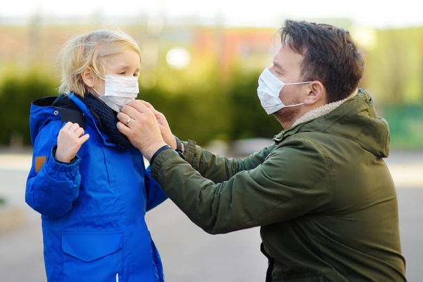 Father wearing a protective mask puts a face mask on a his little son on the street before a stroll or other public place while coronavirus epidemic. Safety during COVID-19. New strains of coronavirus. - Foto, imagen