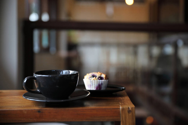Kaffeetasse mit Muffin auf Holztisch in lokalem Café - Foto, Bild