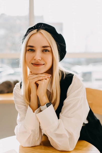Young blonde woman sitting at a cafe table, looking at camera and smiling.  - Foto, immagini