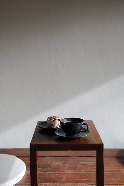 地元のコーヒーショップで木のテーブルの上にマフィンとコーヒーカップ - 写真・画像