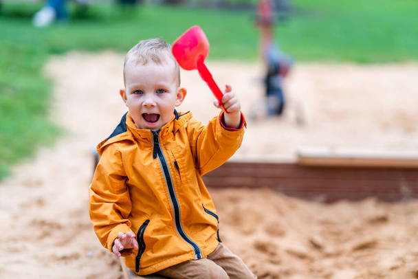 Toddler Sitting in Sandbox, Waving with Pink Toy Shovel - Enjoying Playground - Photo, Image