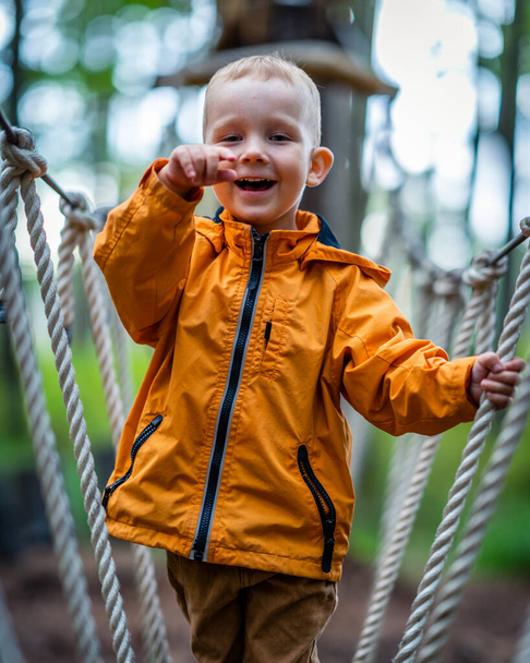 Smiling Kid Pointing to Camera in Woods, Playing on Rope Track - Enjoying Childhood - Photo, Image