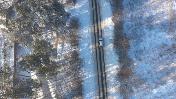 White car riding through snowy rural road. Following to SUV driving at beautiful countryside route on wintry day. Winter holidays journey at nature. Concept of family travel. Aerial shot Top View. - Photo, Image