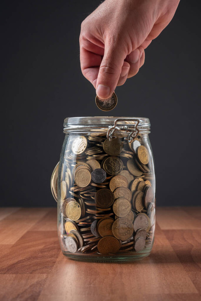 Eine Person legt Münzen in einen Behälter voller Geld - Foto, Bild
