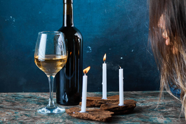 Женщина задувает свечи бокалом белого вина и бутылкой на мраморном столе - Фото, изображение