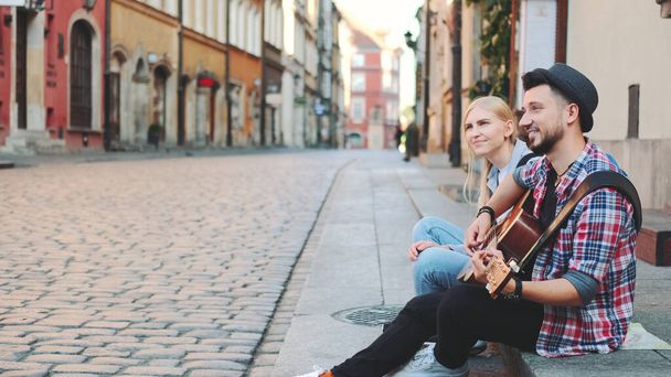 Touristes assis sur le trottoir, jouant de la guitare et se reposant - Photo, image